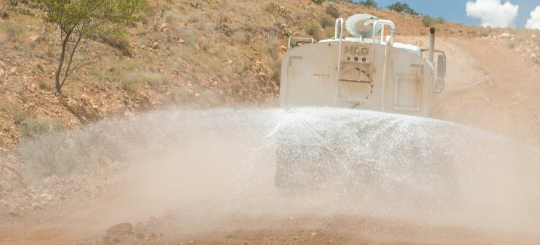 Camión cisterna alejándose del espectador rociando agua en un camino de tierra para equipo pesado