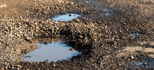 Baches llenos de agua en un camino sin pavimentar que necesita reparaciones